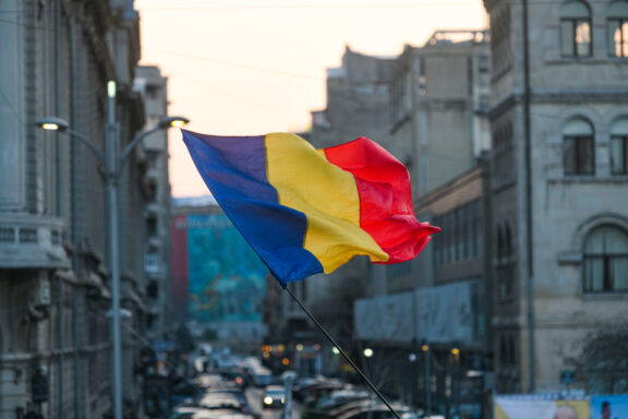 Romanian flag waving in front of a city street at dusk.