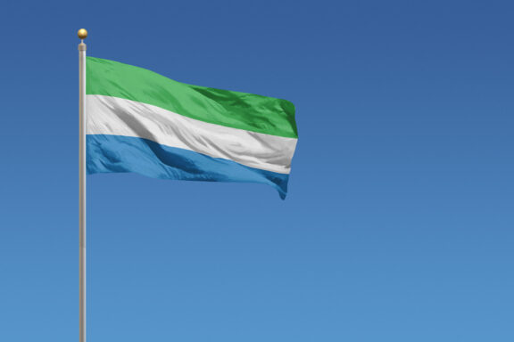 Flag of Sierra Leone waving against a clear blue sky.