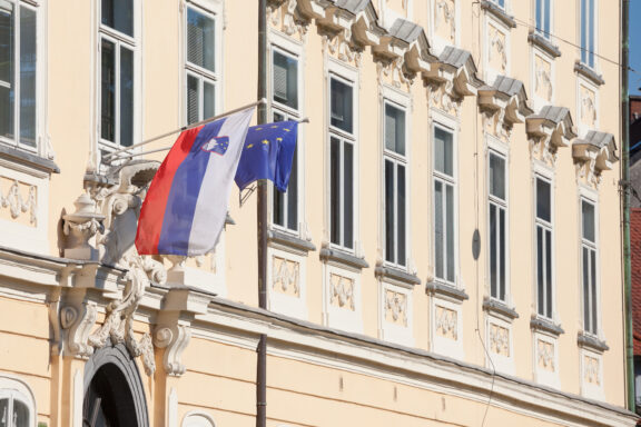 Slovenian flag alongside the European Union flag hanging on a building with classical architecture.