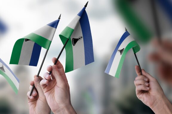 Several small Lesotho flags being waved against a blurred background.