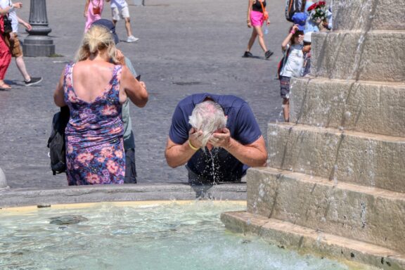 A man splashes water from a fountain in his face on a hot day.