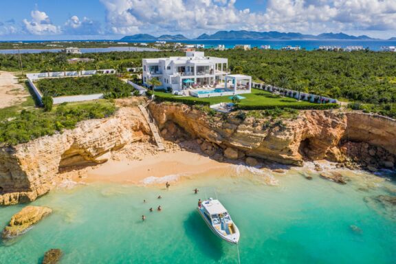 An aerial view of a luxury villa atop a small cliff overlooking the water.