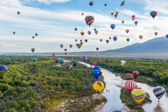 Many colorful hot air balloons hover over the landscape in Bernalillo County, New Mexico.