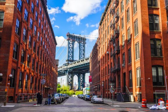 Brick buildings lining a small street frame a view of the Manhattan Bridge and Empire State Building in New York’s King County.