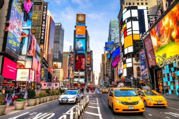 Taxis and a police car drive between towering neon signs in New York City’s Times Square.