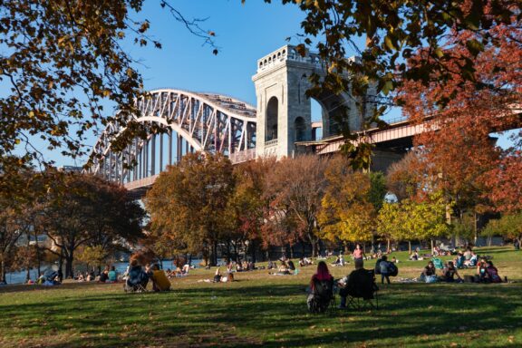 People sit on the grass between the trees in Astoria Park, Queens County.