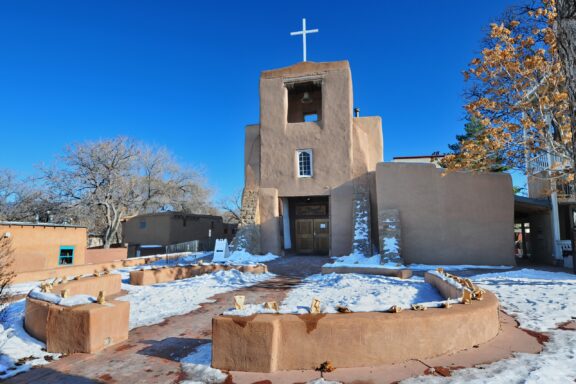 The ground outside the San Miguel Mission Chapel is partly covered with snow.