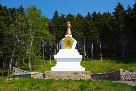 The white and gold Stupa of Enlightenment stands before a group of trees at Gampo Abbey, one of the top meditation centers in the world. 