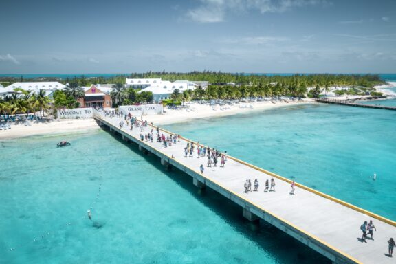 People walk along a long dock extending into turquoise waters from Grand Turk Island.