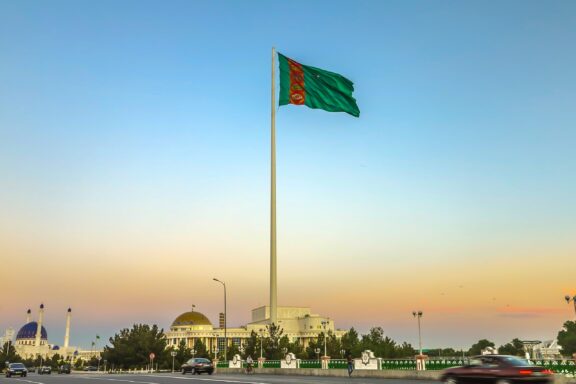 A large Turkmenistan flag waving on a tall flagpole against a twilight sky.