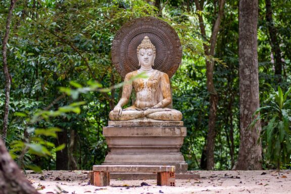 A stone statue of Buddha sits among trees in a forest.