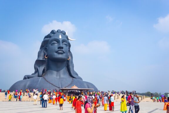 People in colorful clothing gather in front of a giant Shiva statue at Isha Yoga Center in Coimbatore, India. 