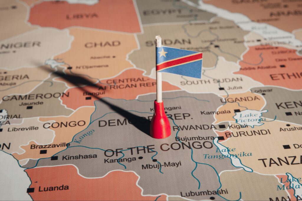 A pushpin on a map highlighting the location of the Democratic Republic of the Congo, with the country's flag above it.