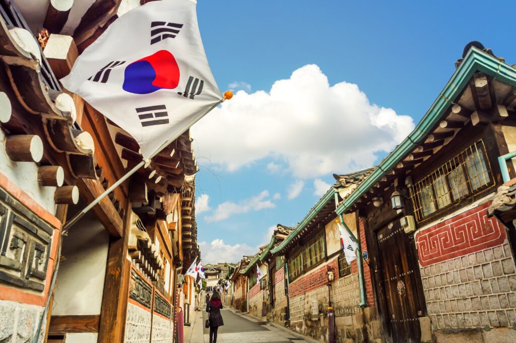 South Korean flag fluttering above the traditional Bukchon Hanok Village with clear blue sky.