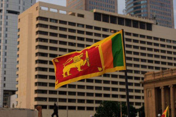 The flag of Sri Lanka waving in front of modern buildings.