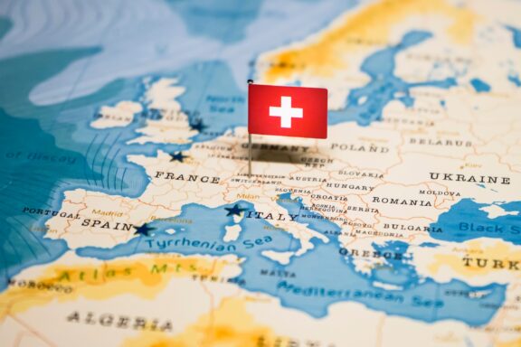 A Swiss flag pin placed on Switzerland on a world map, highlighting the country's location in Europe.