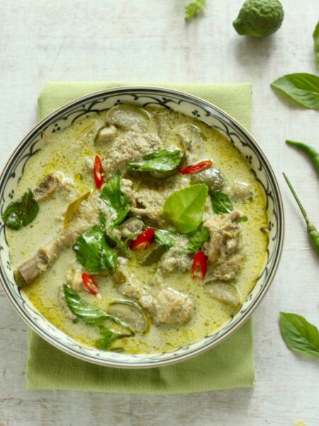 Thai Chicken Green curry, made from chicken, green chilli and eggplant garnished with slice red fresh chilli, Basil leaf. The dish arranged among the spices and herbs.