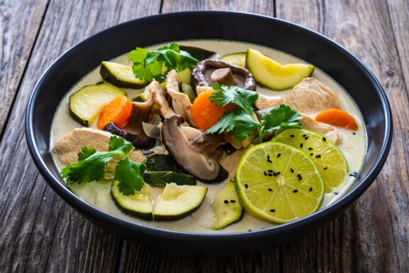 Tom Kha Gai soup - Thai soup with chicken breast nuggets and noodles on wooden table.