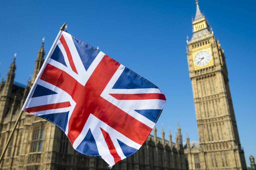 Union Jack flag waving in front of the Big Ben and the Houses of Parliament in London.