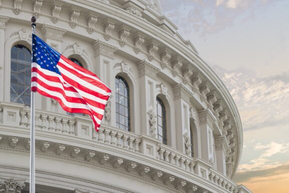 American flag waving in front of the United States Capitol building at sunset.