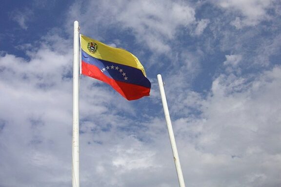 Venezuelan flag waving against a blue sky with clouds.