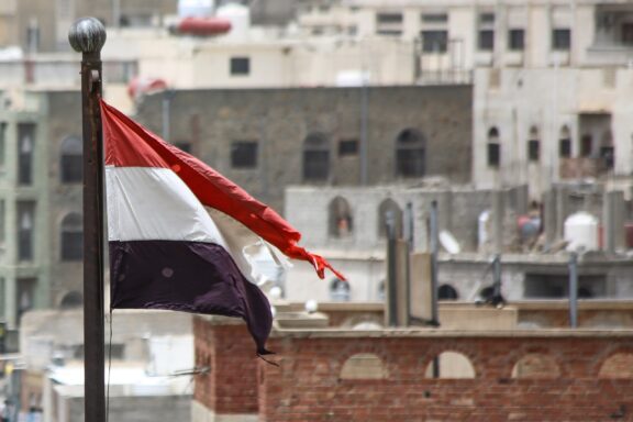 A tattered Yemeni flag fluttering against a backdrop of weathered buildings.