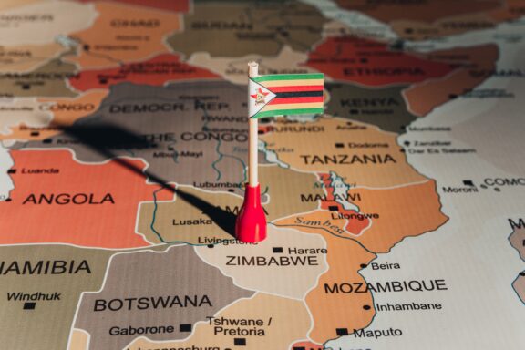 A map of Southern Africa highlighting Zimbabwe with a red pin and a miniature Zimbabwean flag.