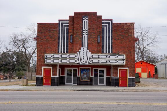 A vintage brick movie theater with an Art Deco facade and marquee against a cloudy sky.