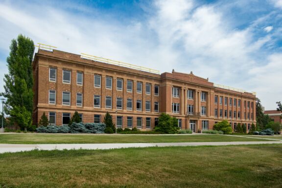 A large brick building with classic architectural features, large windows, and landscaping, under a partly cloudy sky.