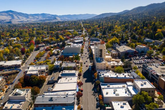 Aerial View of a Tree-Lined Street in Ashland, Oregon with Surrounding Buildings and Mountains in the Distance Aerial view of a tree-lined downtown street in Ashland, Oregon with buildings on either side, surrounded by autumn-colored foliage.