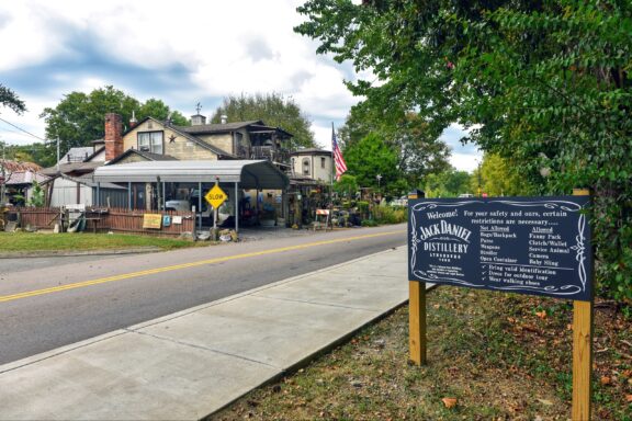 A street view of a rustic building with signs indicating the entrance to the Jack Daniel Distillery, with an information board outlining visitor restrictions and requirements.