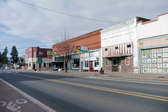 A quiet street scene in a small town with a row of old, single-story storefront buildings.