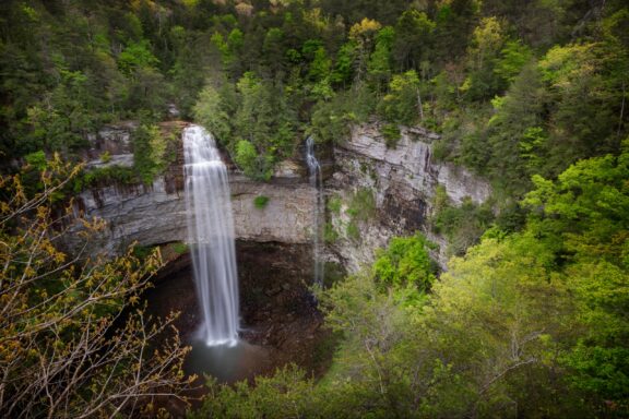 Aerial view of a tall waterfall cascading down a cliff surrounded by lush green forest.