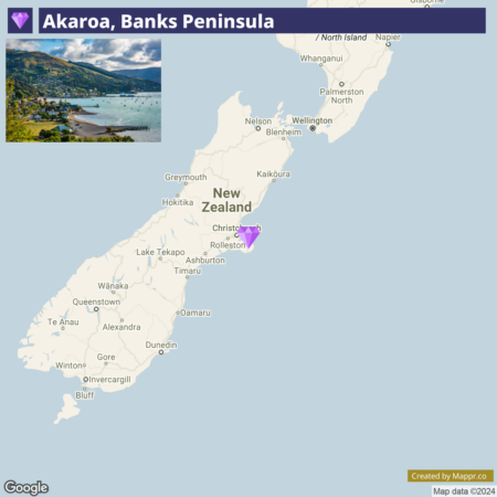 "Map of New Zealand focusing on the South Island with a purple pin marking Akaroa on the Banks Peninsula, southeast of Christchurch. An inset photo in the upper left corner shows a scenic view of the coastal town of Akaroa with lush green hills and the blue waters of the bay."