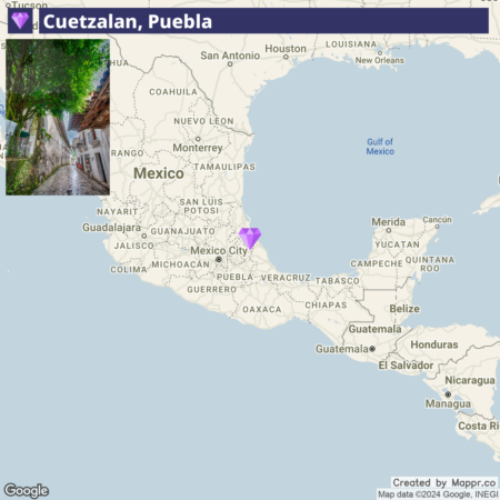 An interactive map highlighting the location of Cuetzalan, Puebla in Mexico, with an inset picture in the top left corner showing a narrow cobblestone street lined by white buildings with red tile roofs and lush green trees overarching the pathway.