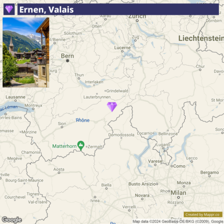 A map centered on Switzerland with a focus on the region of Valais, marked by a purple pin near the labeled town "Ernen." The Matterhorn mountain and the city of Zermatt are also indicated to the south. An inset photo in the upper left corner shows a view of traditional Swiss chalets in Ernen. The map includes other Swiss cities, such as Bern and Lucerne, and parts of neighboring countries Italy and Liechtenstein.