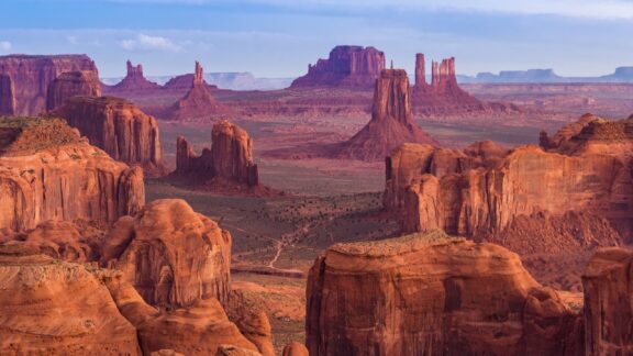 Stunning view of Monument Valley with iconic sandstone buttes and mesas under a clear sky at sunset.