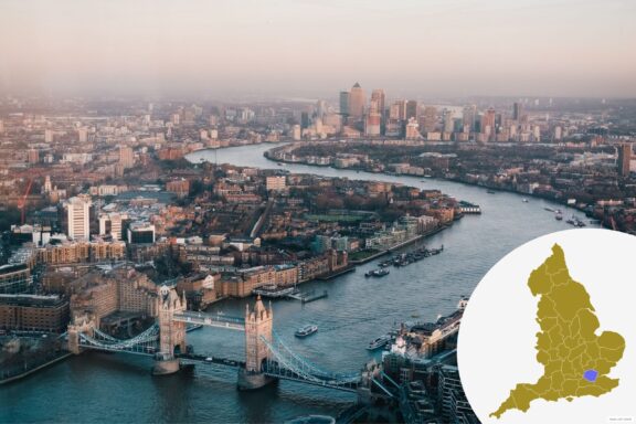 Aerial view of London during sunset with Tower Bridge in the foreground, the River Thames winding through the city, and the modern Canary Wharf skyline in the distance. A small map of the UK in the lower right highlights London's location with a blue area.