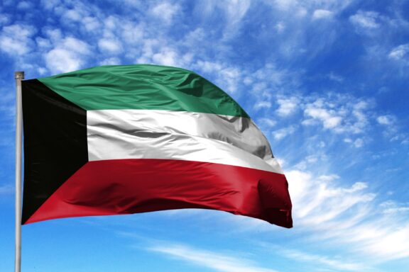 A Kuwaiti flag waving against a cloudy blue sky.