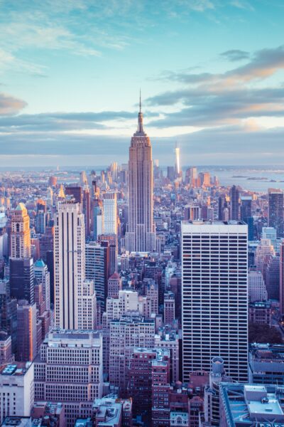 Aerial view of the New York City skyline at dusk, featuring the Empire State Building and other skyscrapers, with a soft golden and blue sky in the background.