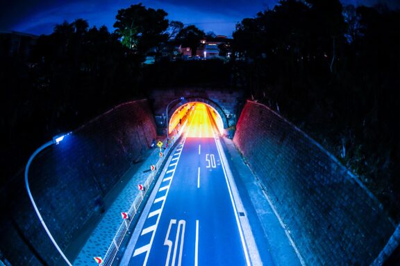 A night view of a road leading into the Yamate tunnel with light trails from vehicles and a speed limit sign showing "50" painted on the road surface.