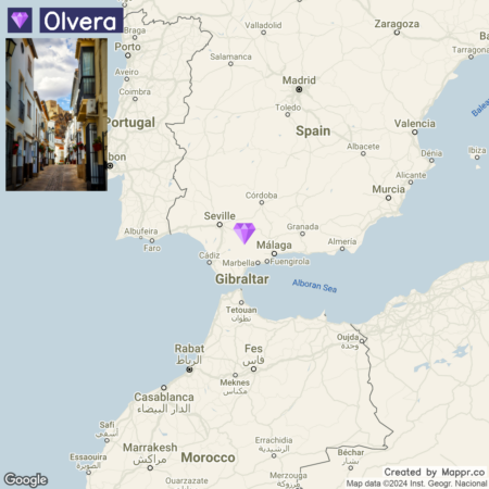 A split view image with the left side showing a charming street in the town of Olvera, Spain, with traditional white houses and a clear blue sky, and the right side displaying a map highlighting the geographic location of Olvera in southern Spain near other cities and the Mediterranean Sea. There's a purple location marker on Olvera in the map, and a Google watermark with map data attribution at the bottom right corner.