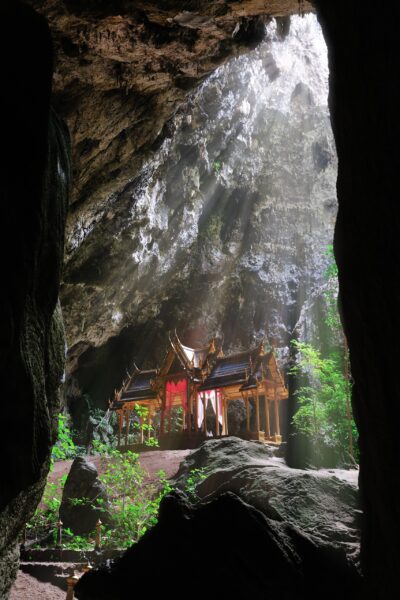 A traditional Thai pavilion within a large cave, illuminated by natural light streaming in from an opening above.