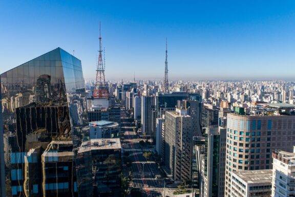 Aerial view of a dense urban skyline of São Paulo, Brazil with modern skyscrapers, broadcast antennas, and clear blue skies.