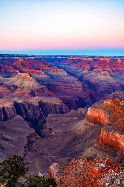 Alt text: A vibrant sunset over the Grand Canyon, highlighting the red rock formations and deep gorges against a colorful sky gradient.