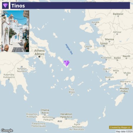 A map highlighting the Greek island of Tinos in the Aegean Sea, with a small inset image in the top left corner showing a picturesque street view of Tinos, featuring white buildings with blue doors and windows, decorated with flowers. The map also shows surrounding geographic locations such as Athens and other Aegean islands.