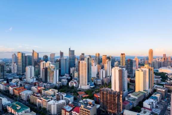 A panoramic view of a densely built-up Makatim cityscape near Manila with numerous high-rise buildings under a clear blue sky during golden hour.