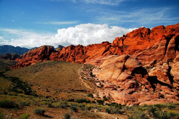 Vivid red rock formations with striations under a blue sky with fluffy clouds.