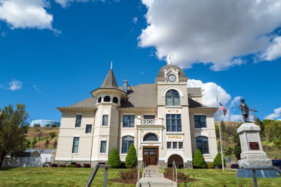 Historic Victorian-style courthouse building with clock tower, featuring "Garfield" nameplate, an American flag, and a soldier monument under a blue sky with puffy clouds.