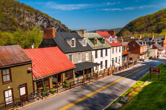 A sunny view of a historic street with colorful buildings and a rocky hill in the background.